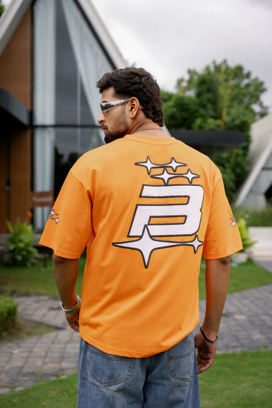 Man wearing an orange t-shirt with a logo, standing outdoors.