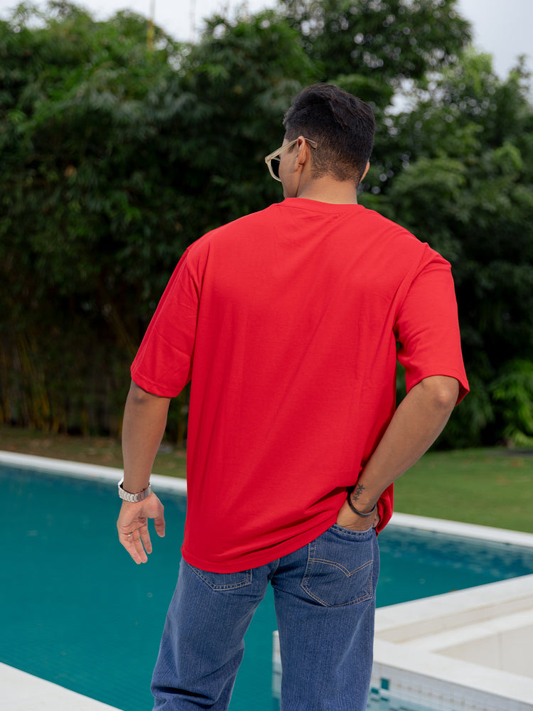 Person wearing a red t-shirt and blue jeans standing by a pool