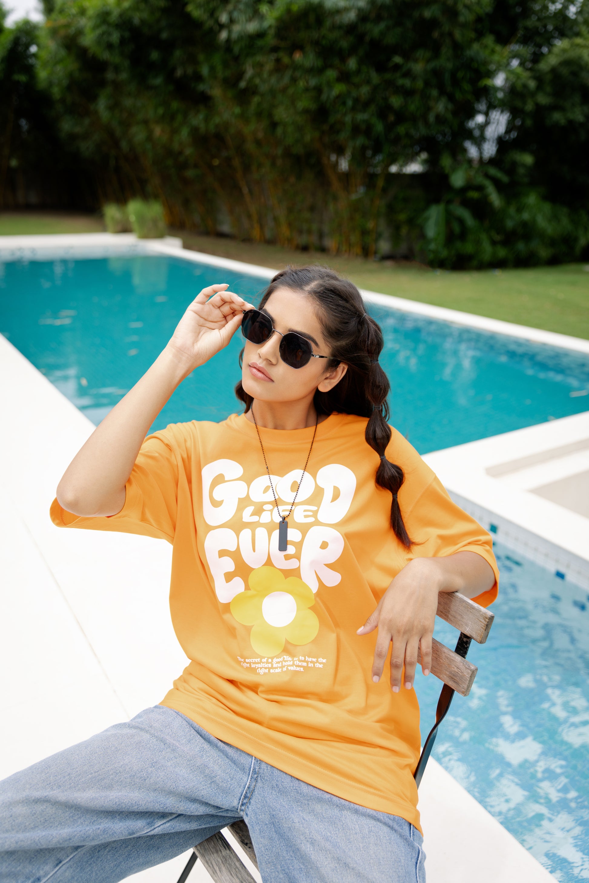 Woman wearing an orange t-shirt with 'Good Life' text by a poolside