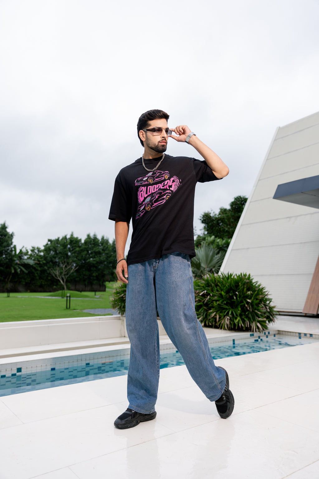 Man wearing a black t-shirt with pink graphics and blue jeans standing by a pool.