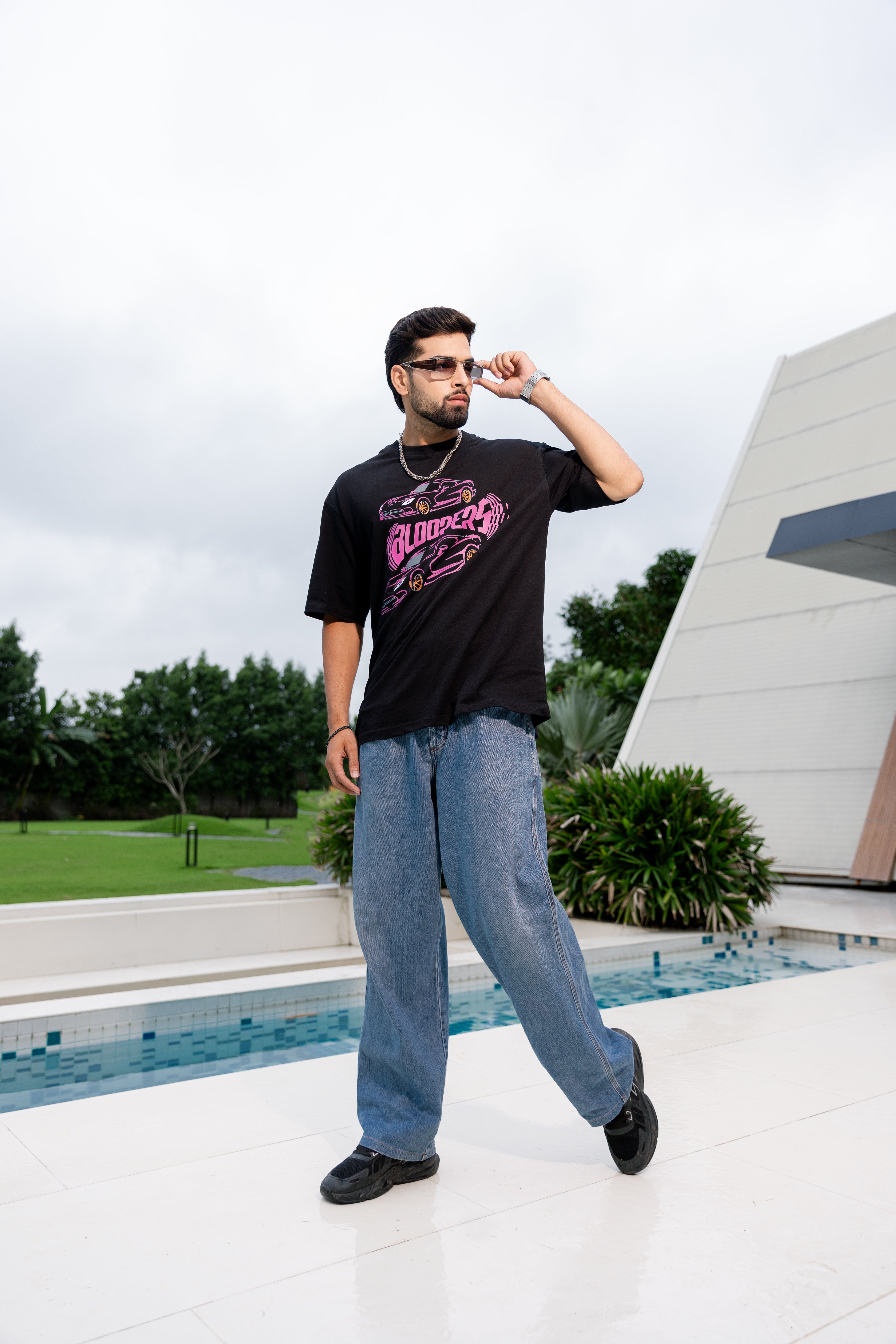 Man wearing a black t-shirt with pink graphics and blue jeans standing by a pool.