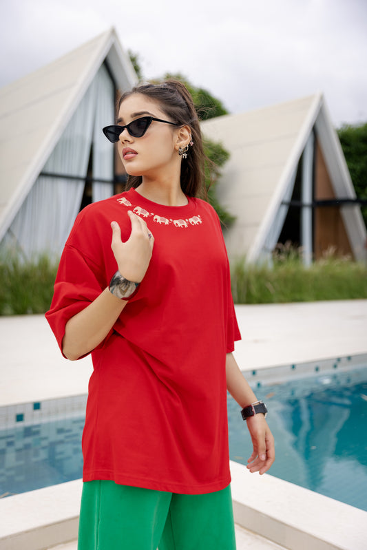 Woman wearing a red oversized t-shirt and green pants standing by a pool