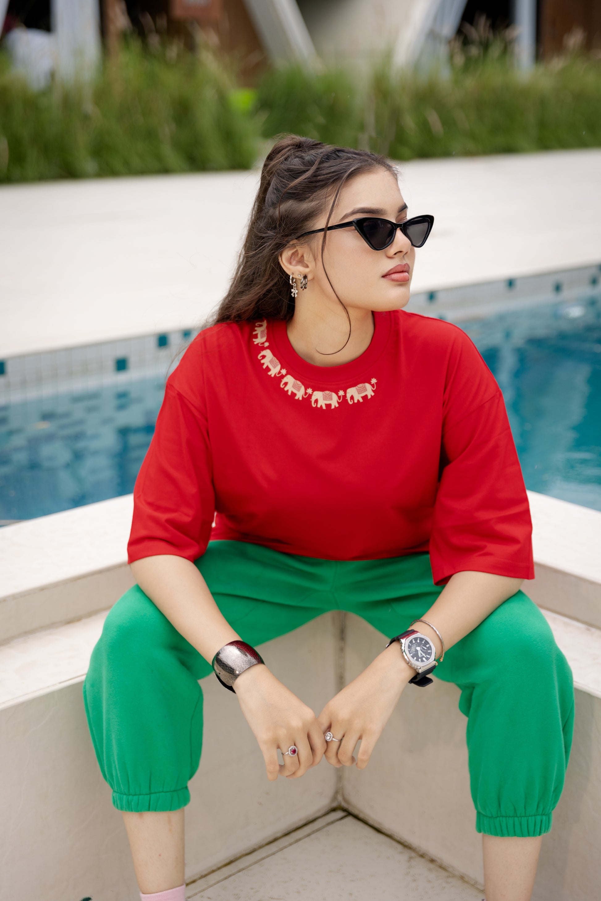 Woman in red top and green pants sitting by a pool