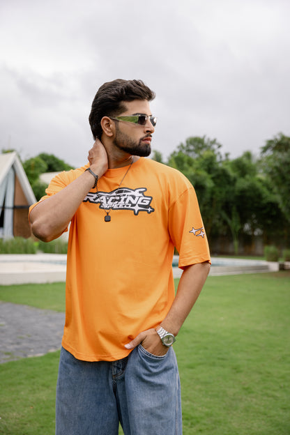 Man wearing an orange t-shirt with a logo, standing outdoors.