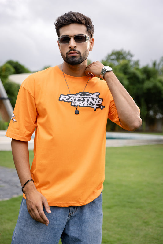 Man wearing an orange t-shirt with a logo, standing outdoors on grass.