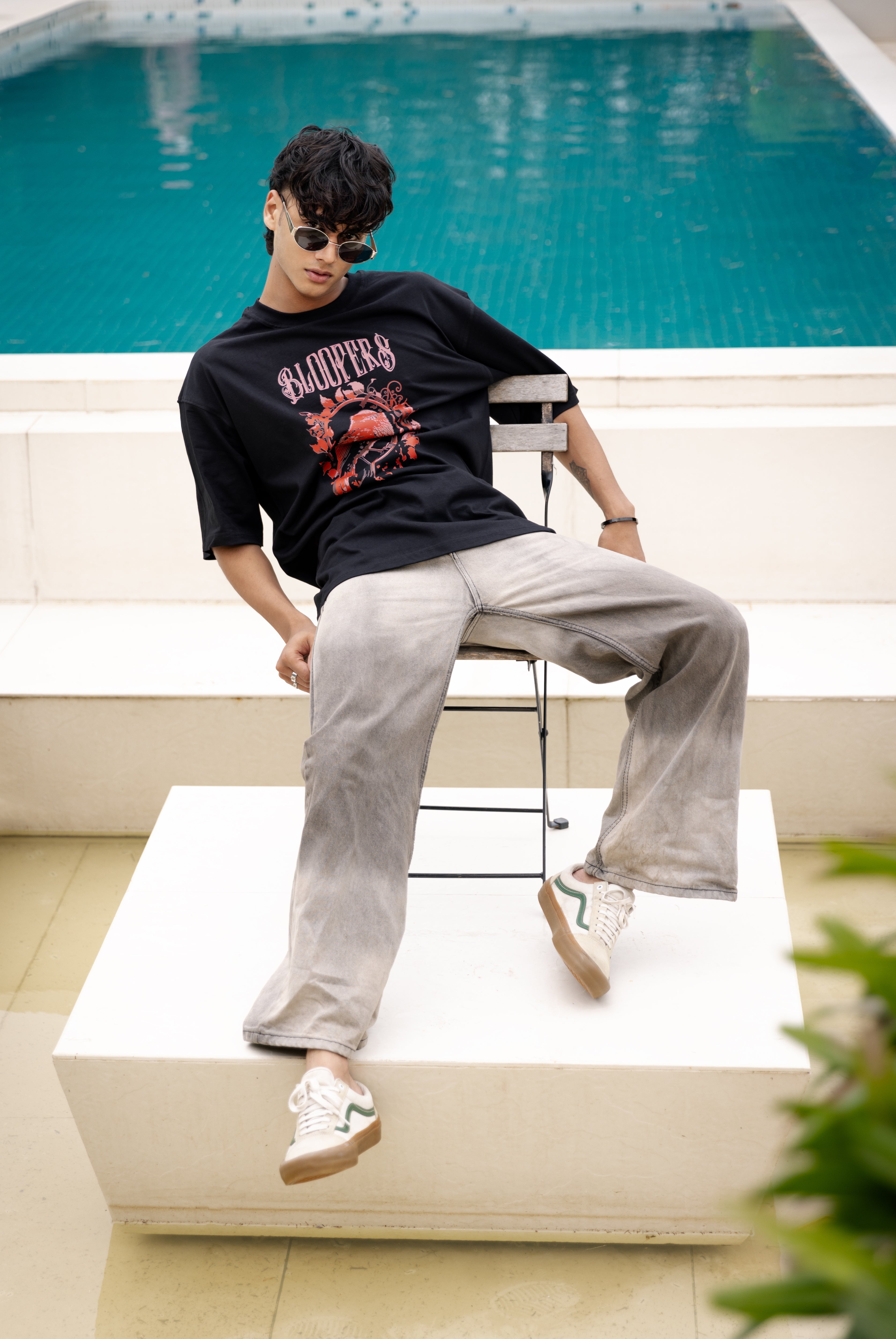 Person sitting on a white chair by a pool wearing a black t-shirt 