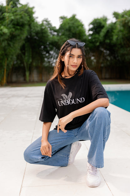 Woman wearing a black 'UNBOUND' t-shirt and blue jeans sitting by a pool.