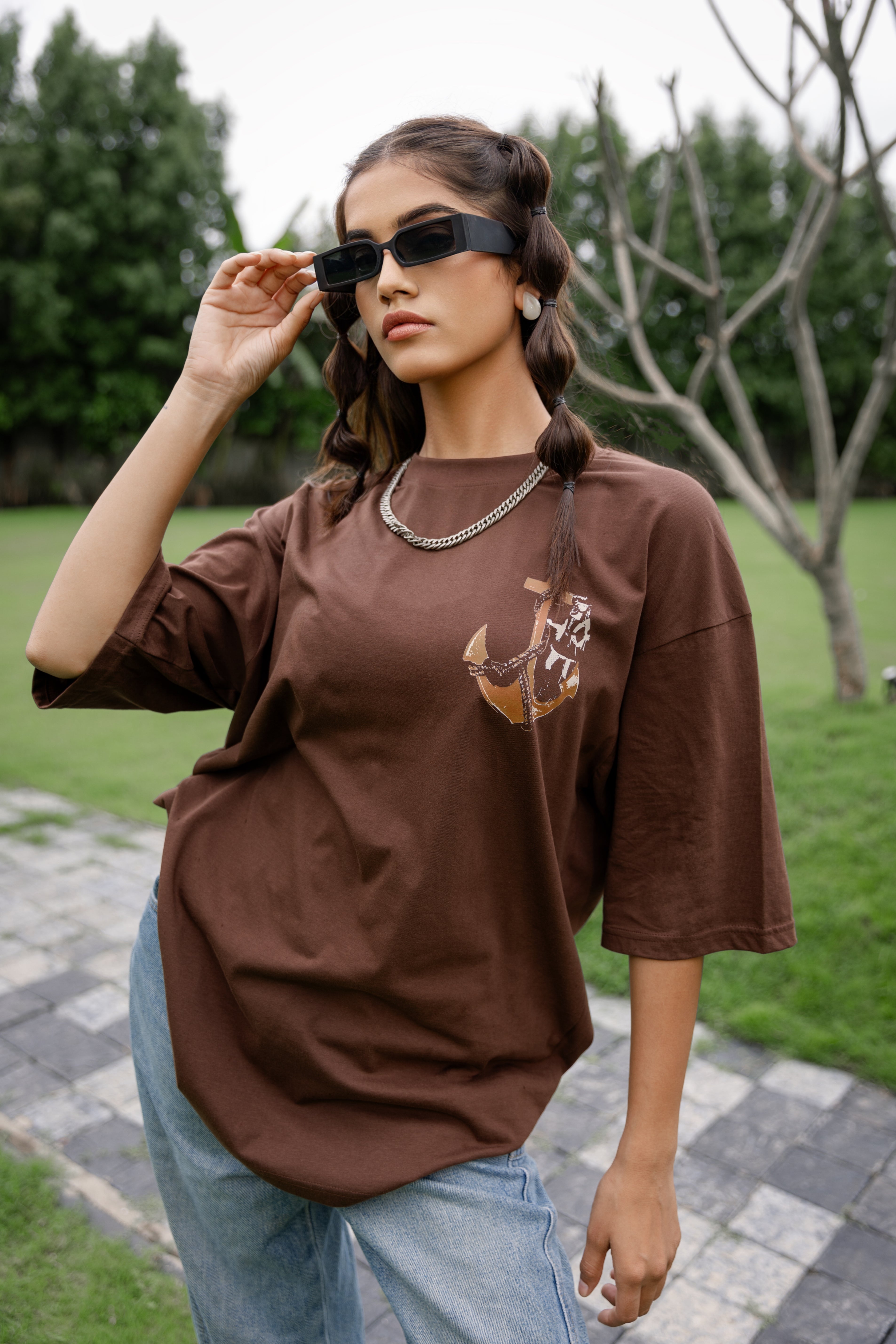Woman wearing a brown oversized shirt with a graphic design outdoors.