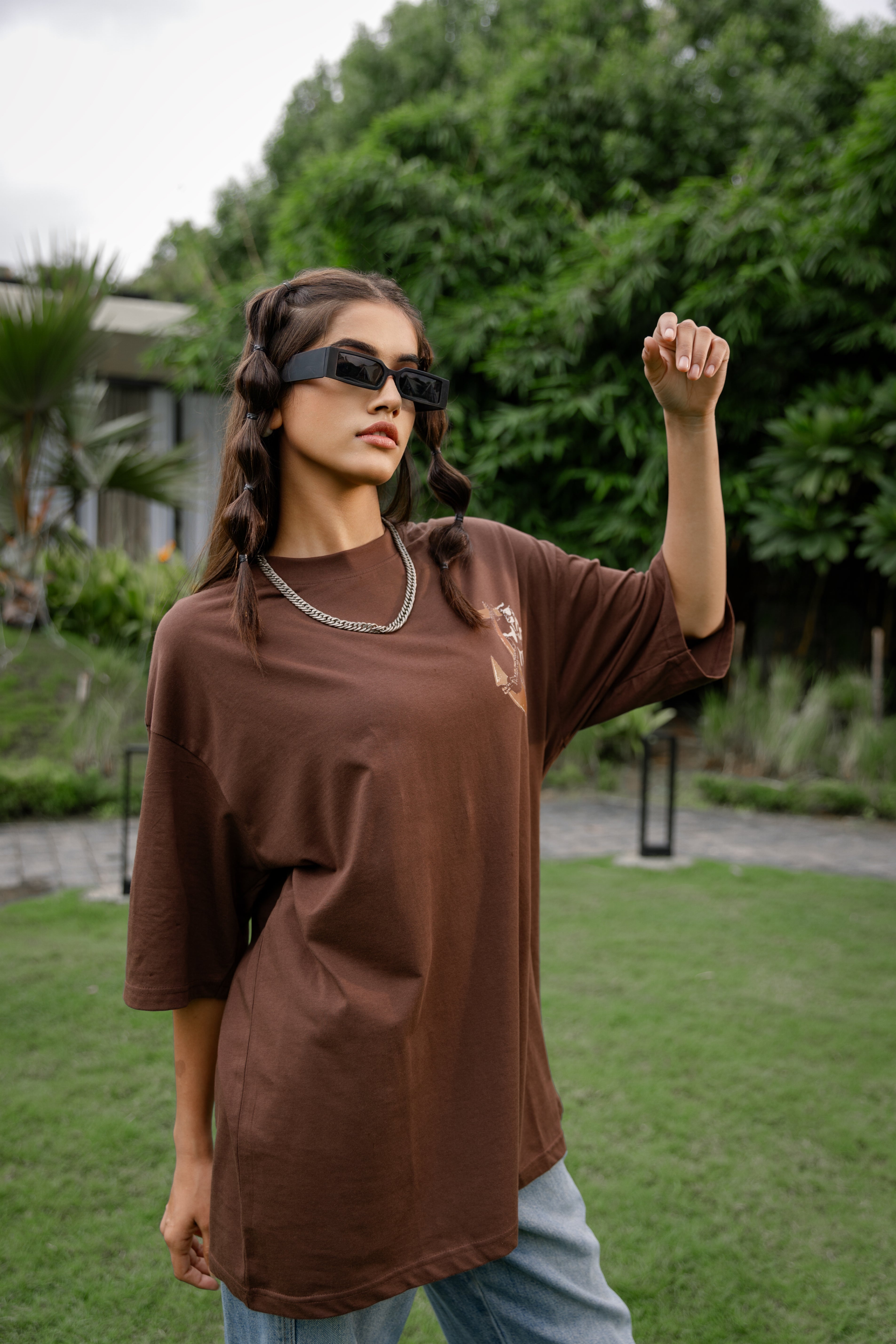 Woman in a brown shirt and sunglasses standing outdoors.
