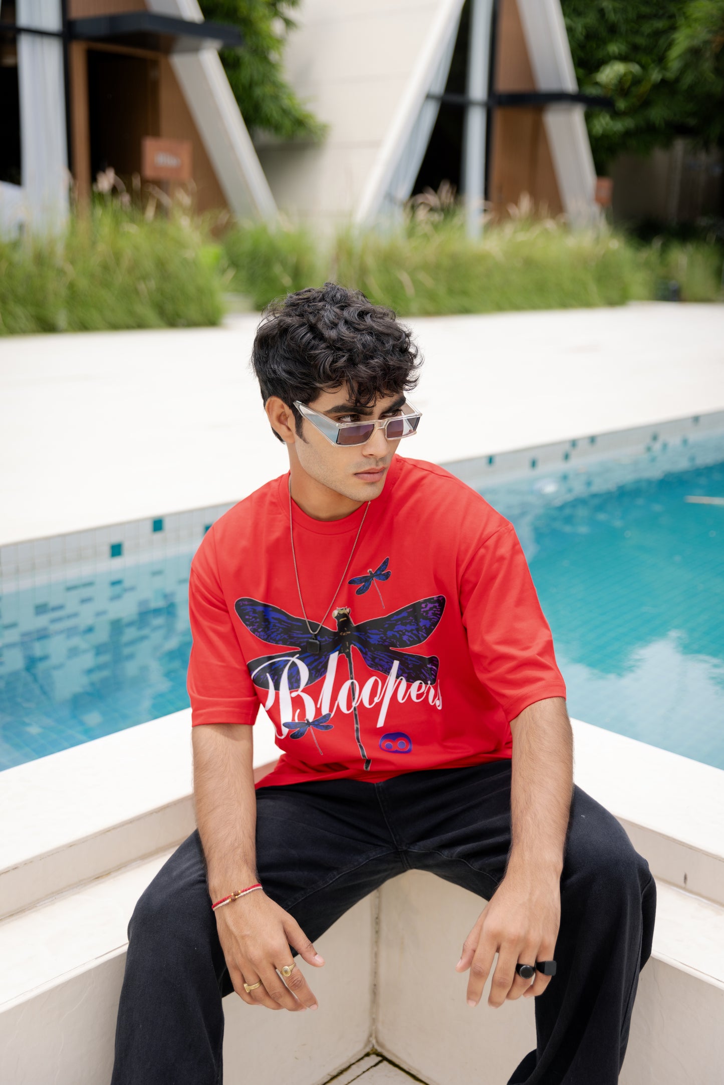 Person wearing a red t-shirt with a butterfly logo sitting by a pool
