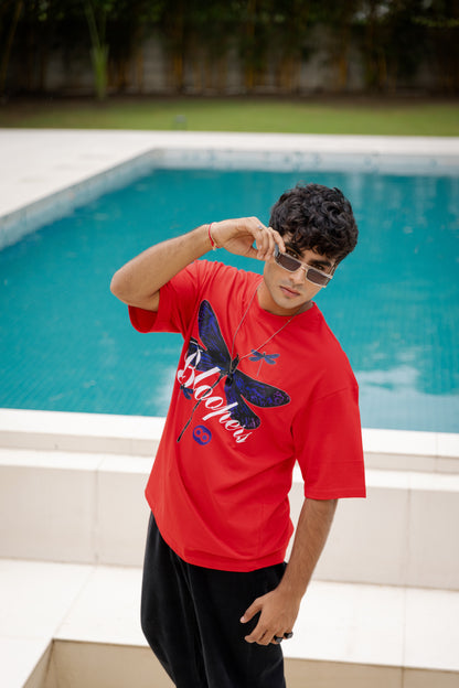 A boy wearing a red t-shirt with a butterfly design by a pool